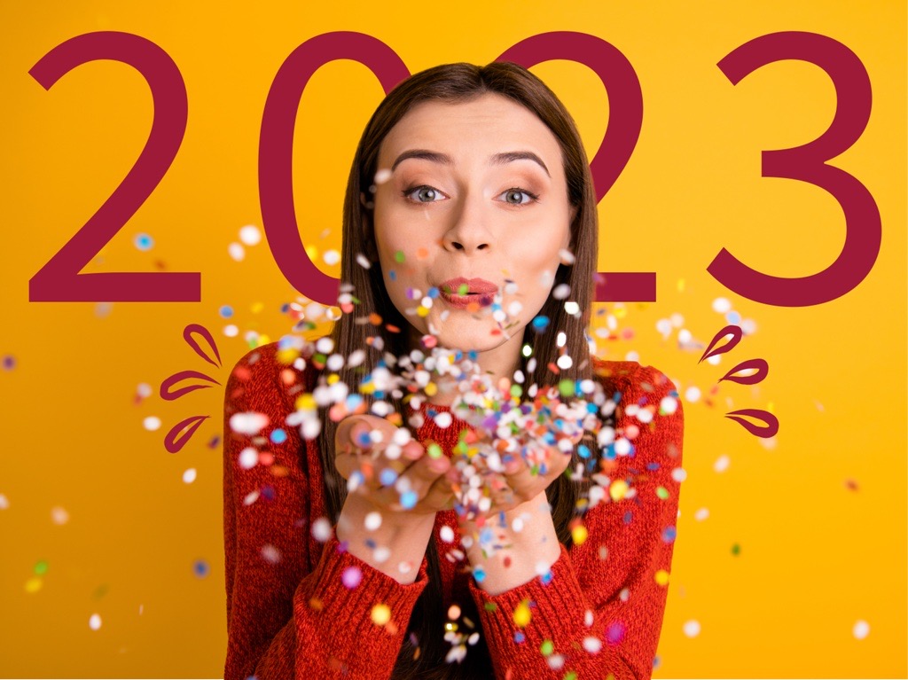 Jeune femme en pull rouge souffle sur des confettis qui s'envolent. 2023 écrit en arrière-plan.